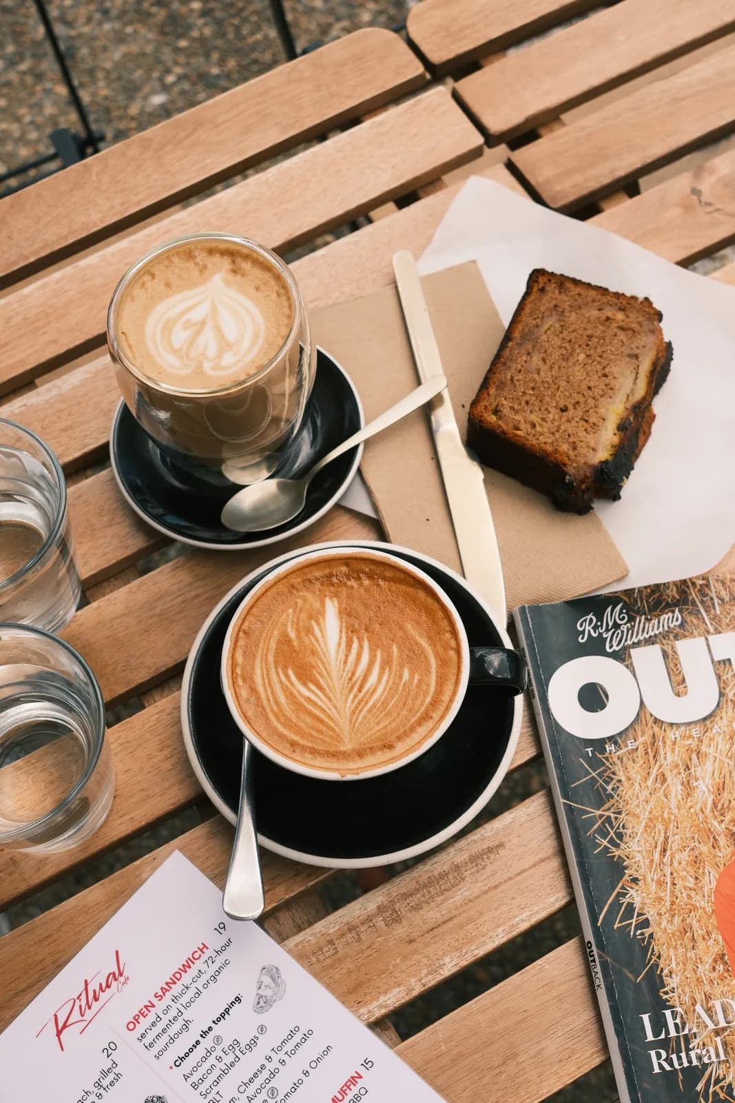Two lattes and a slice of cake on a wooden table.