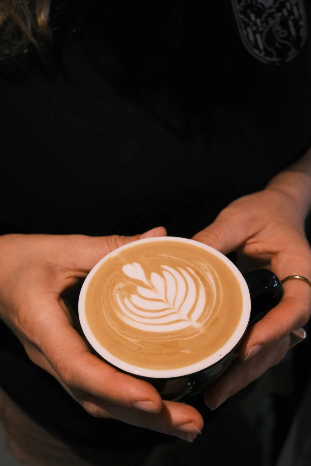 A latte with leaf art in the milk, held in two hands.